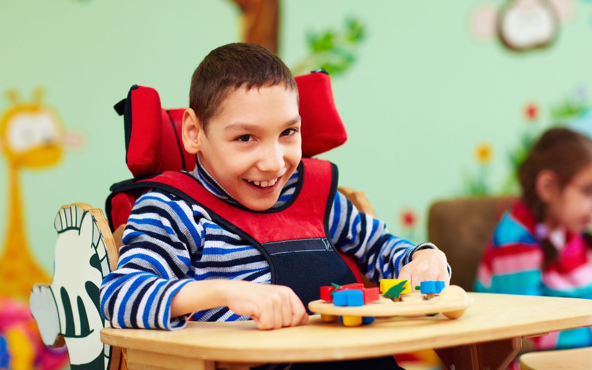 A young boy is sitting in a wheelchair playing with toys.
