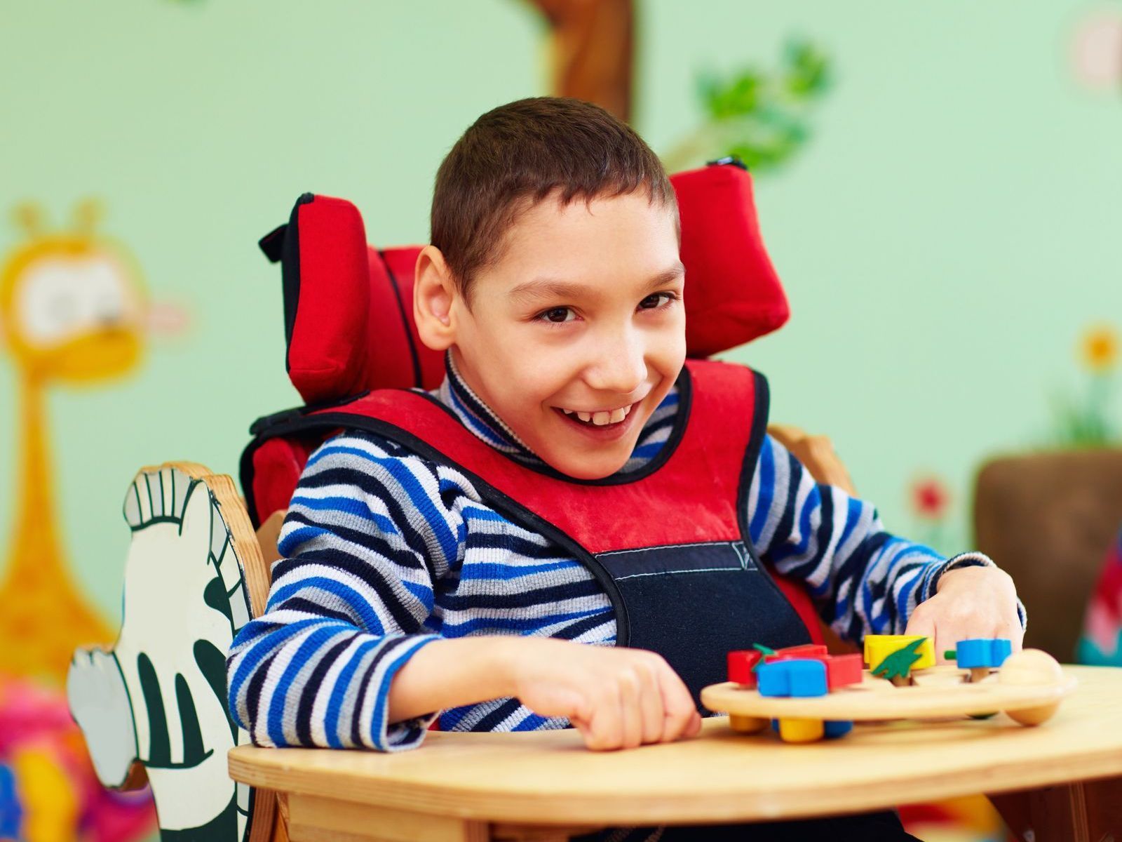 A young boy is sitting in a wheelchair playing with toys.
