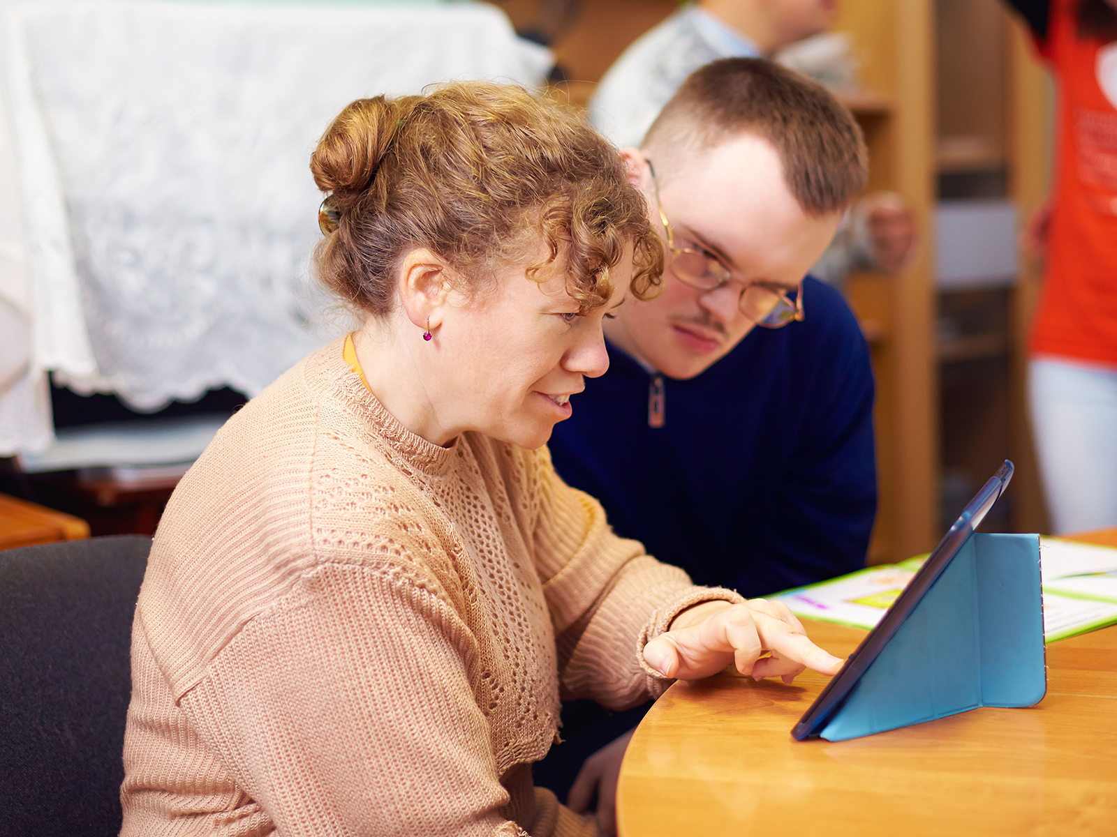 A man and a woman are sitting at a table looking at a tablet.