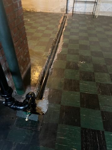 A black pipe is sitting on a checkered floor next to a brick wall.