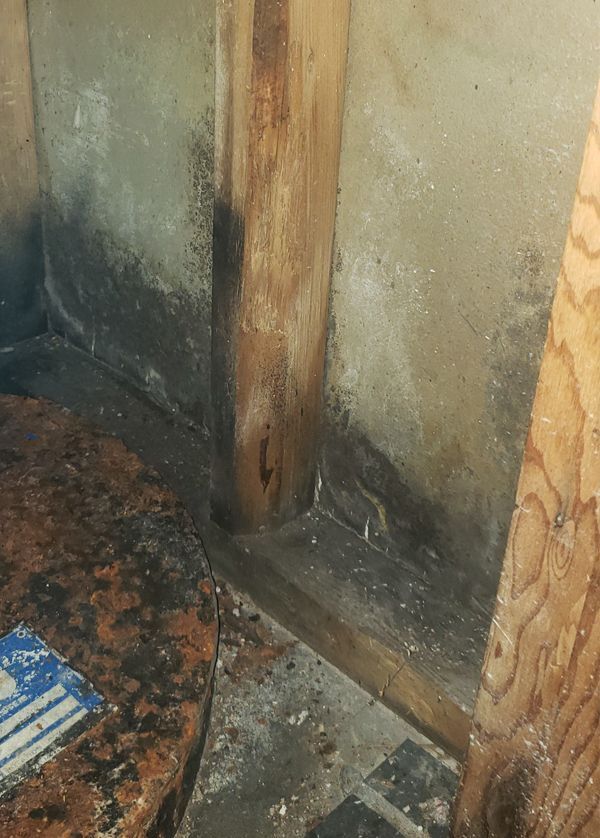 A corner of a room with a hazardous concrete wall and wooden beams.