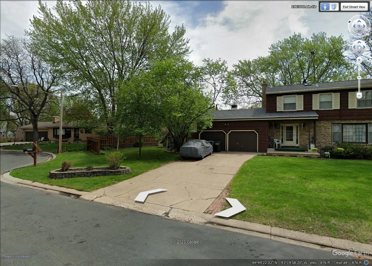 A split-level suburban house with a two-car garage, a concrete driveway, and a large green lawn on a residential street.