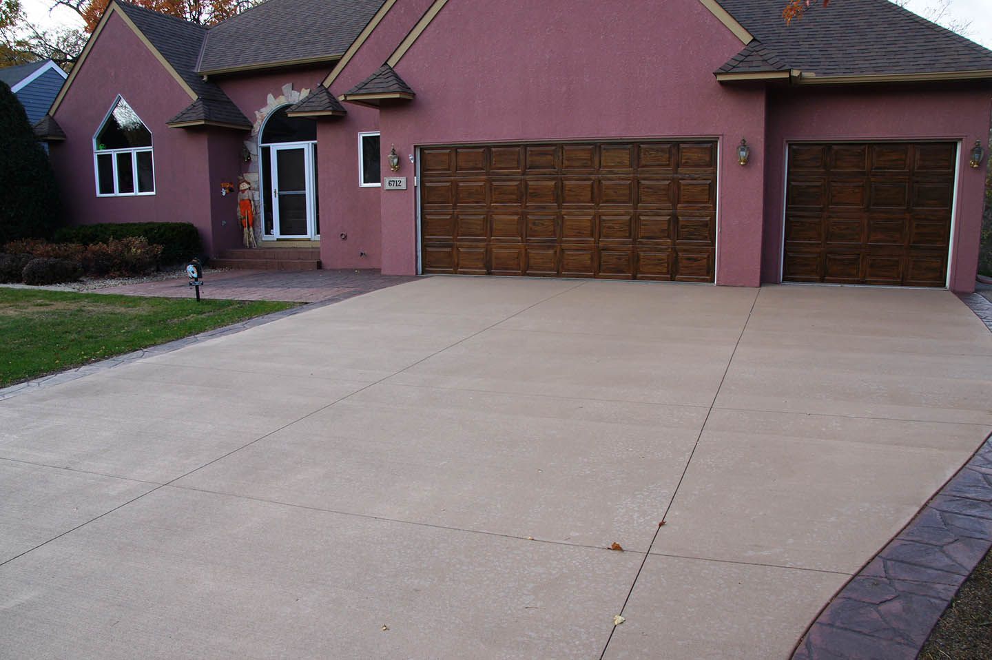 A mauve-colored suburban house with a large, clean concrete driveway and a dark decorative border along the edge.