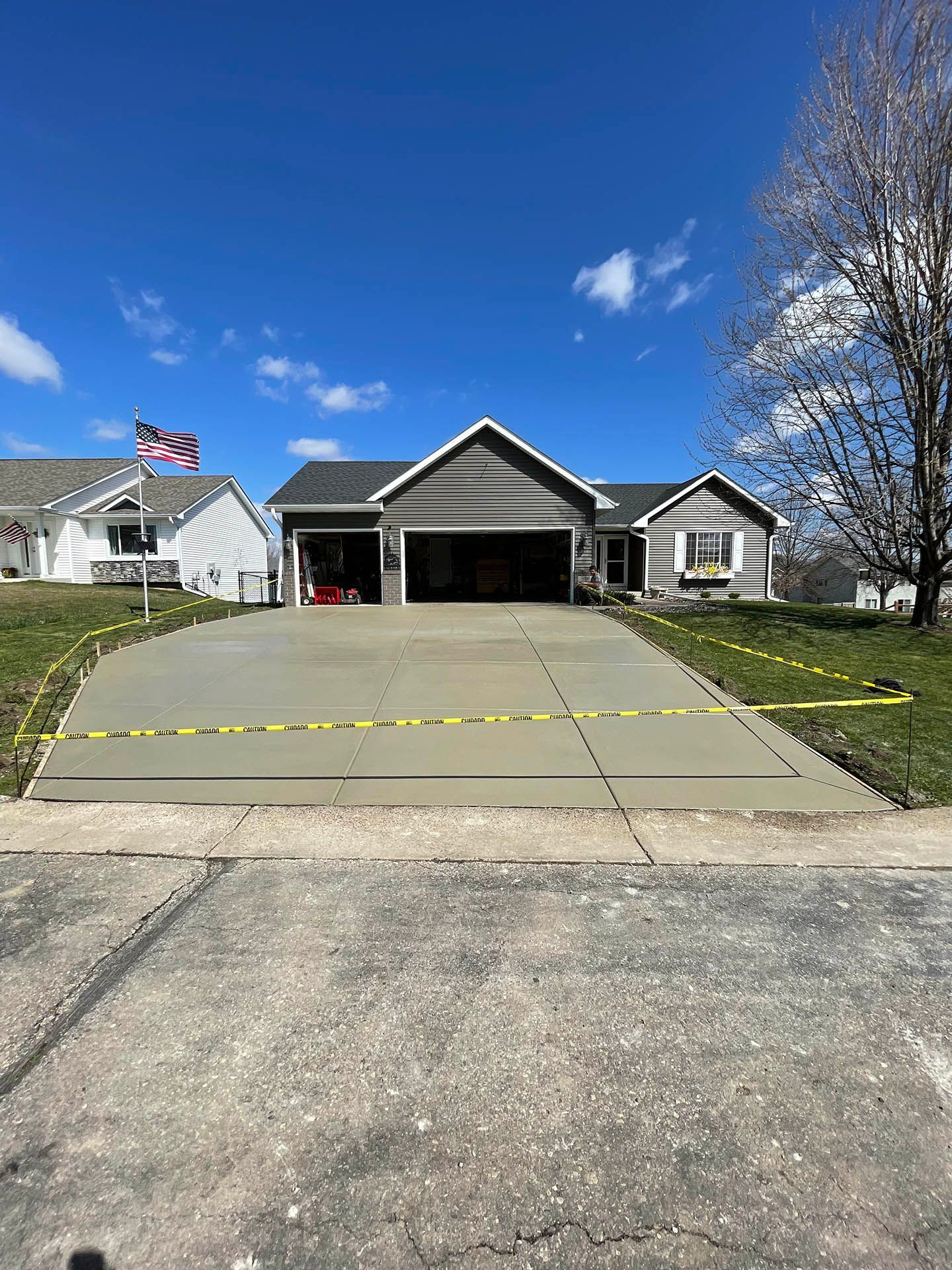 A suburban house with a newly poured concrete driveway blocked off by yellow caution tape under a clear blue sky.