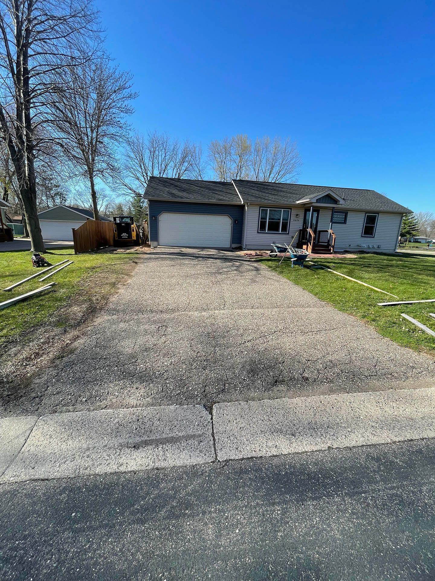 A single-story house with light siding and a dark roof, featuring a wide gravel driveway leading to a garage.