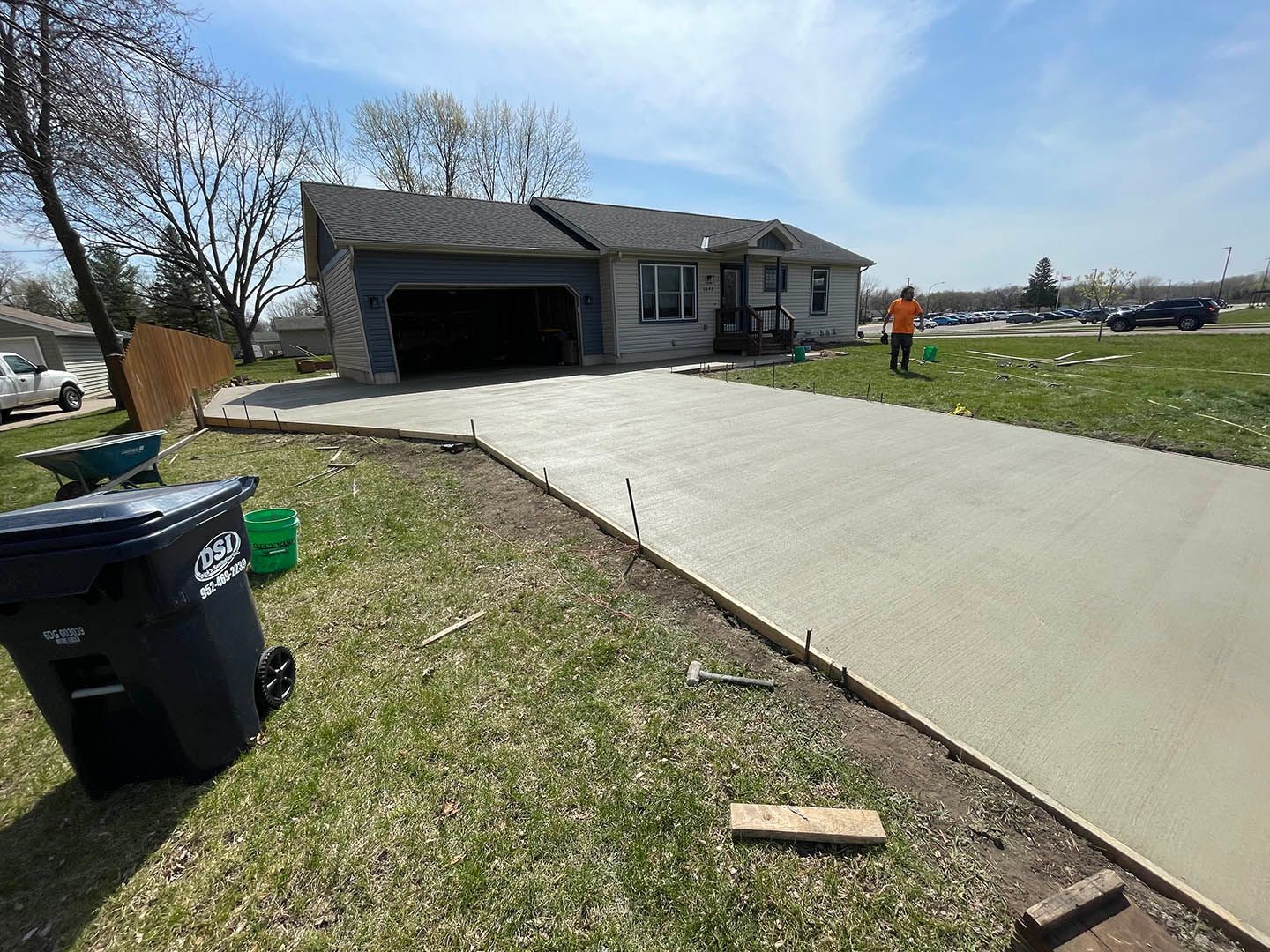 A newly poured concrete driveway leads up to the garage of a single-story suburban house on a sunny day.