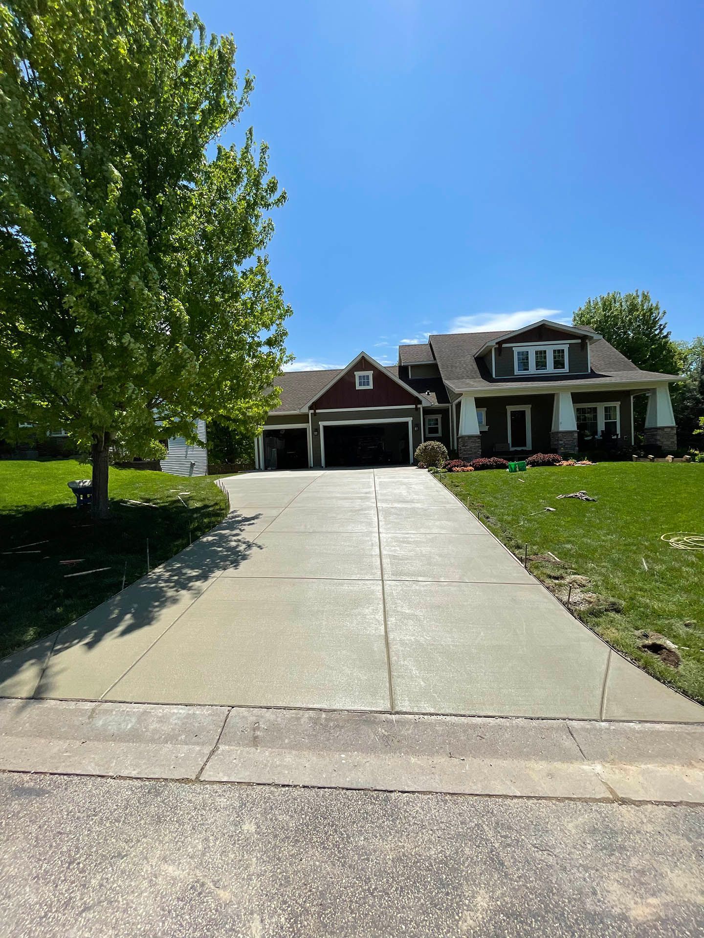 A concrete driveway leads to a house with a dark red garage and brown siding under a clear blue sky.