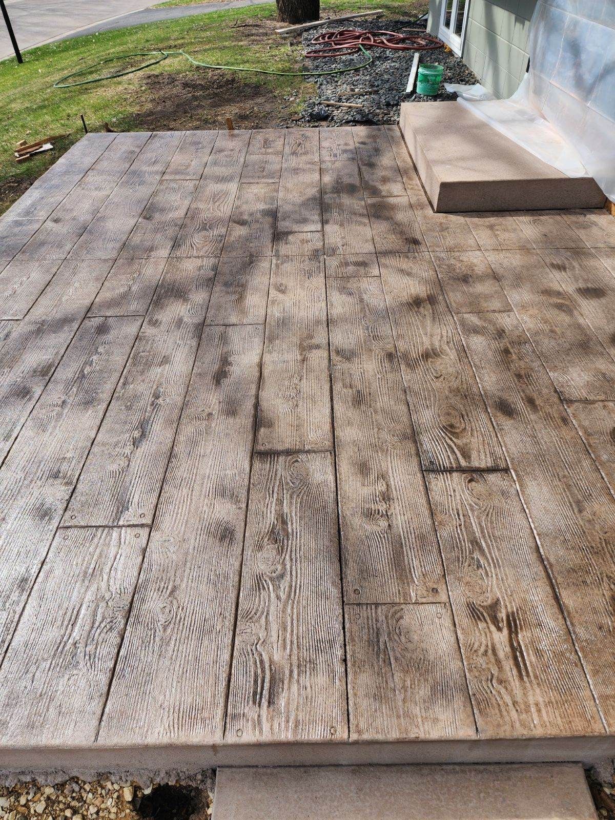 A stamped concrete patio textured to resemble wood planks, featuring a light tan finish with dark brown highlights.