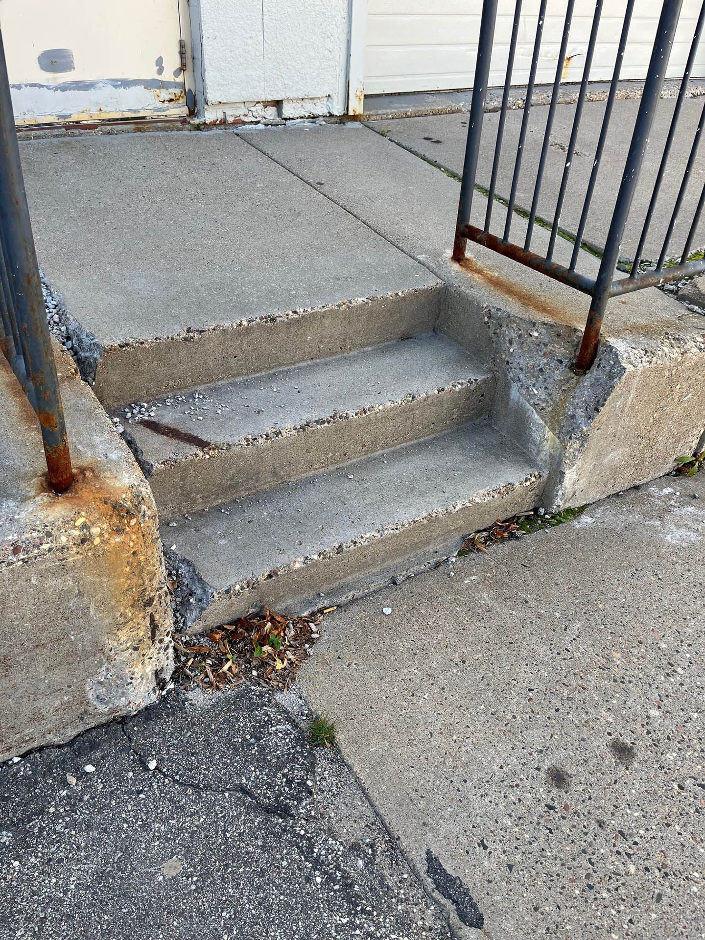 Concrete steps leading to a doorway, flanked by rusted metal railings and showing signs of wear and age.