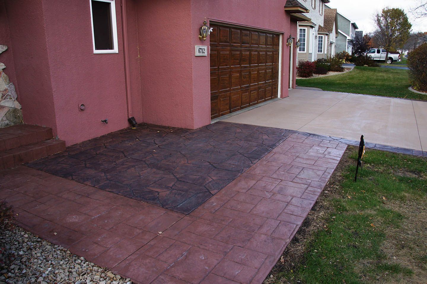 A new stamped concrete walkway and patio area with dark slate and reddish-brown borders next to a pink house and garage.