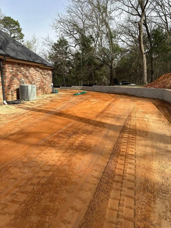 A dirt road leading to a house with a brick building in the background.