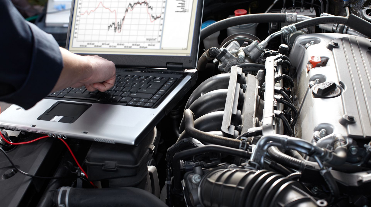 Mechanic uses a laptop connected to a car engine, displaying diagnostic data with graphs.