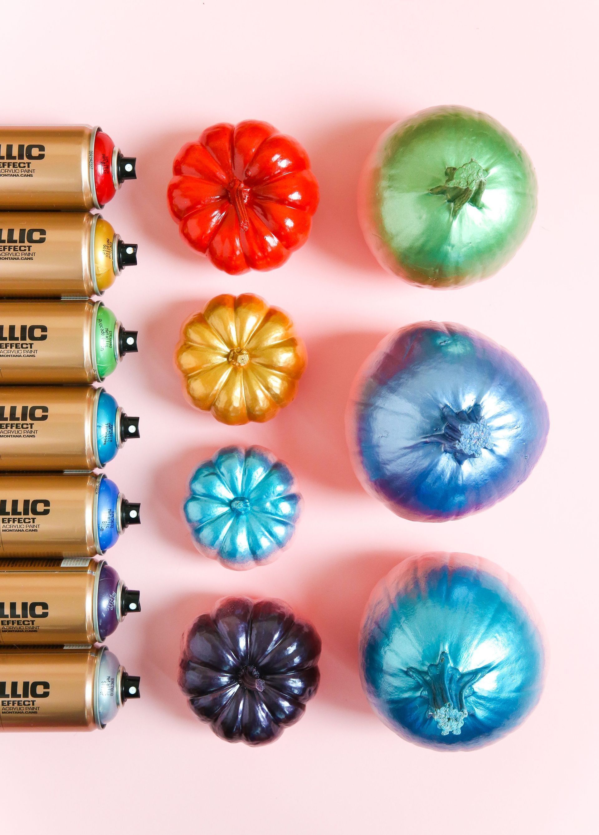 A row of spray painted pumpkins on a pink background.