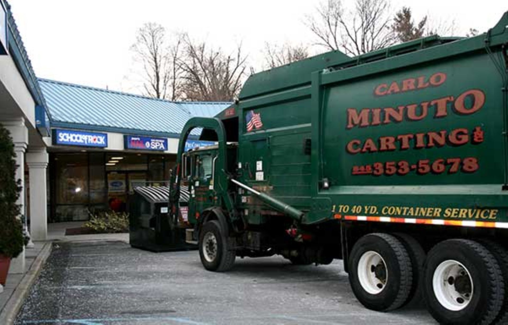 Blue and green industrial dumpsters on a paved path beside trees