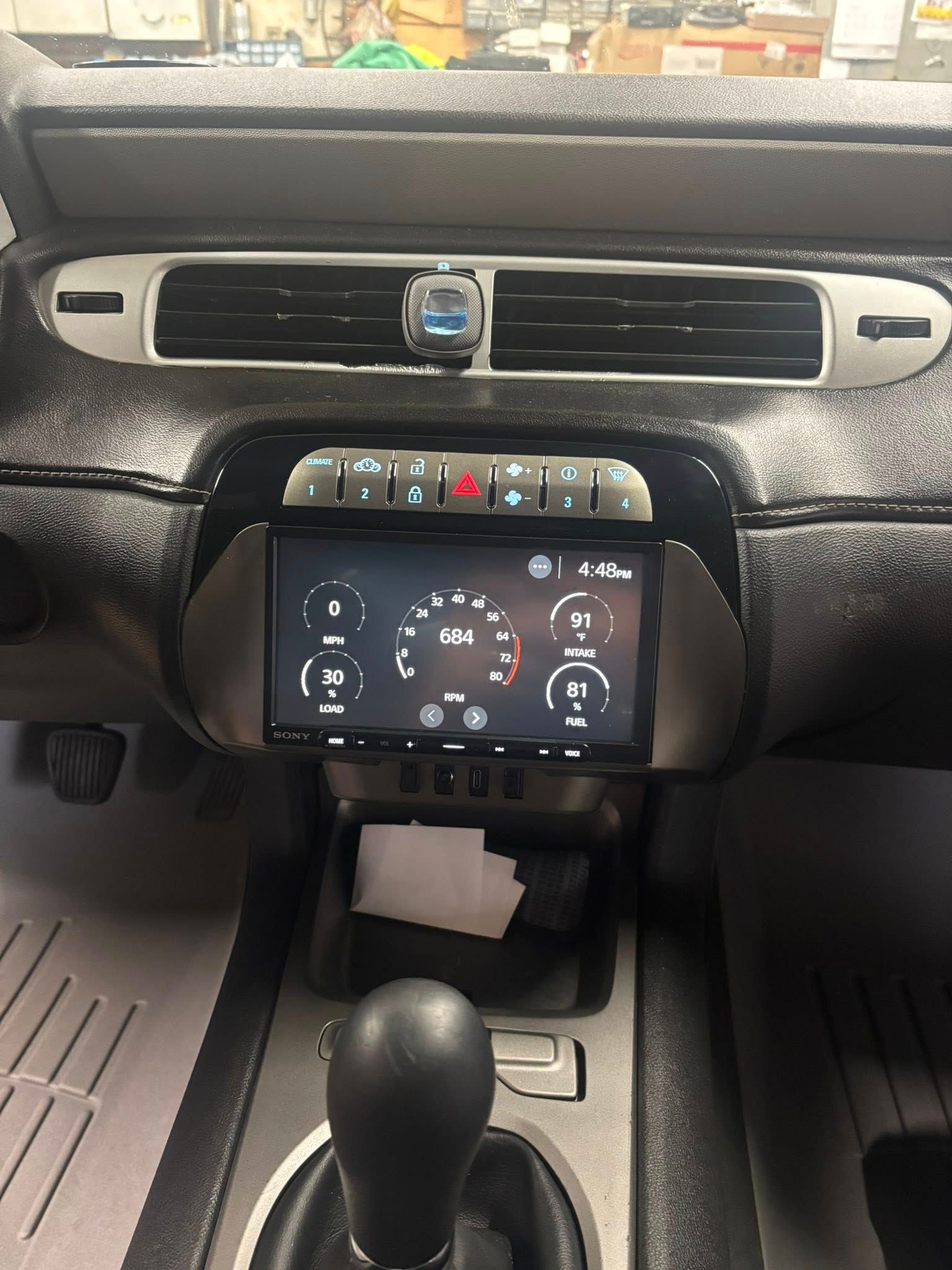 Car dashboard with a large central screen displaying gauges, black interior, and a gear shift.