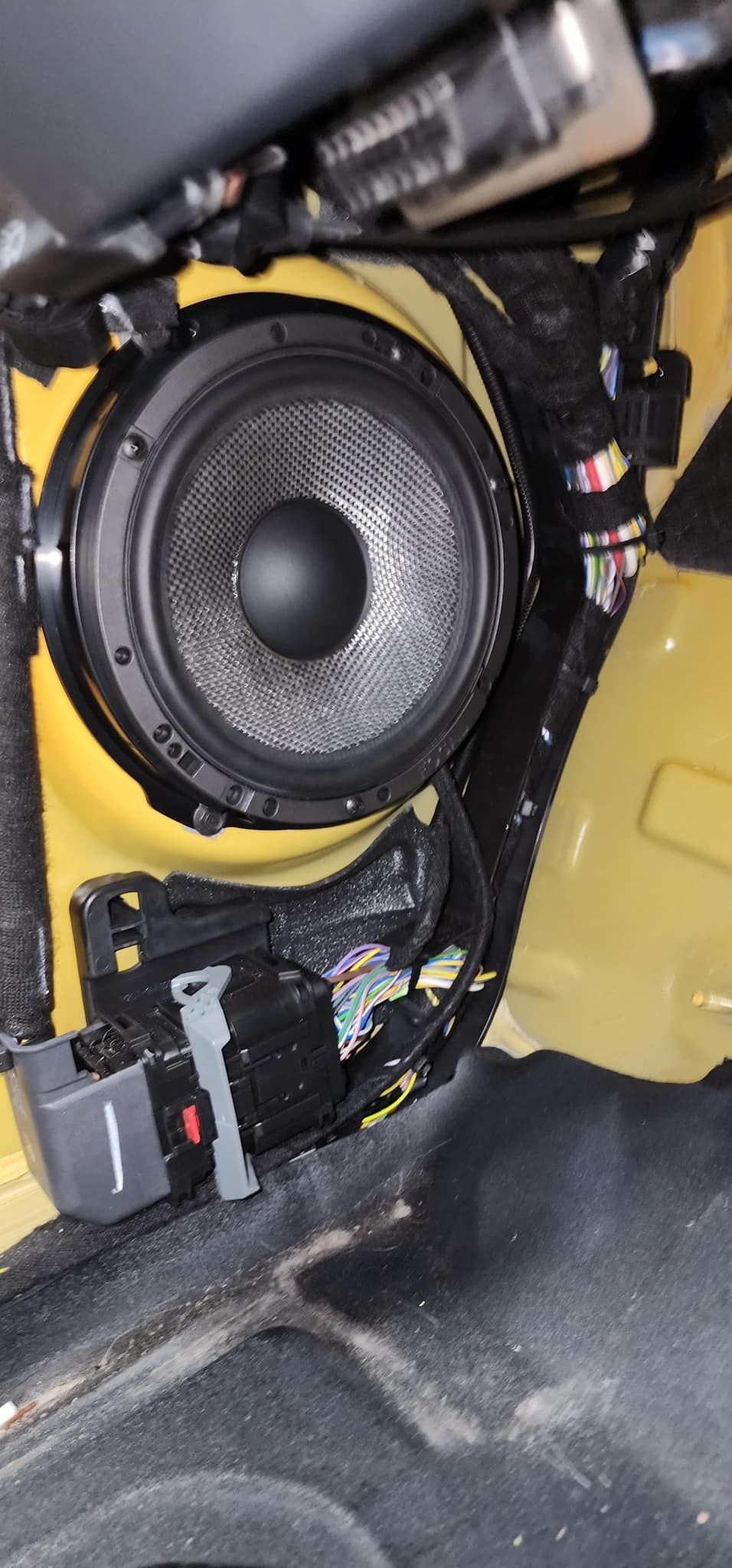 Car audio speaker installed in a yellow interior, with black speaker and surrounding components.