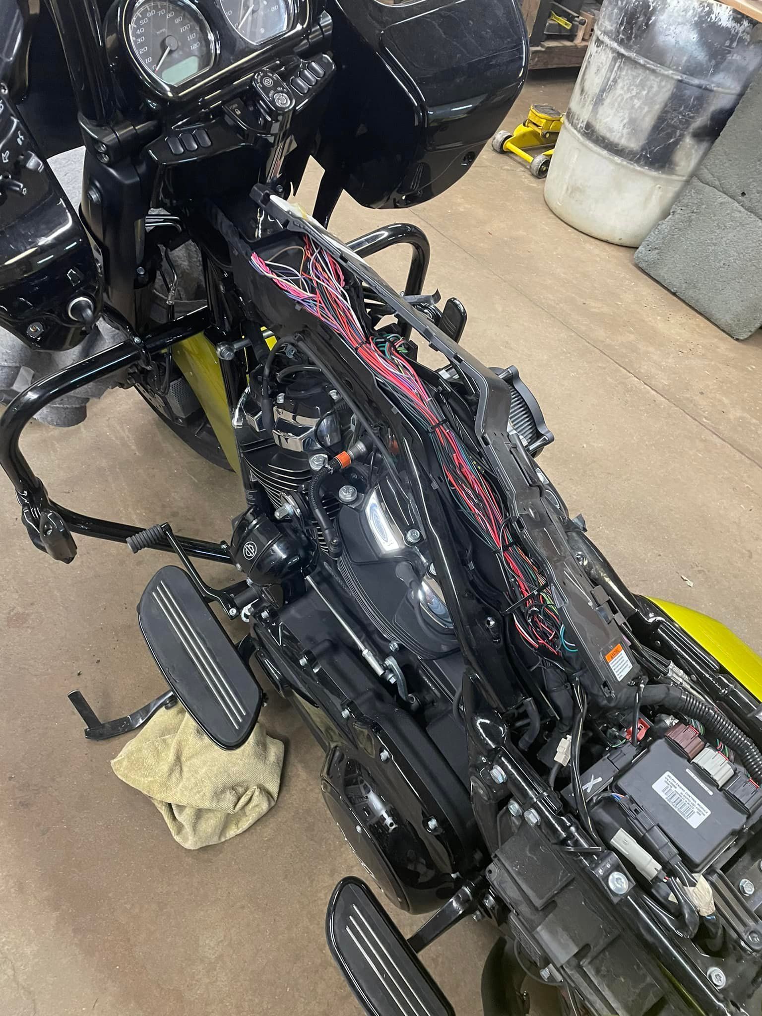 Black motorcycle undergoing repair, exposed engine components, interior shop setting.