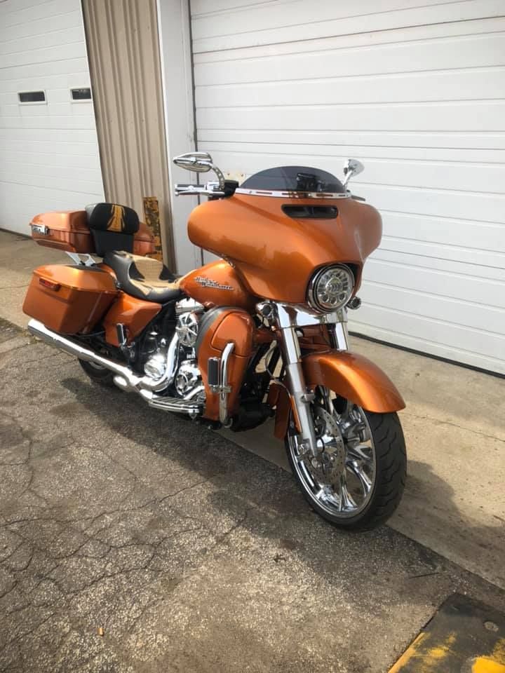 Copper-colored Harley-Davidson motorcycle parked in front of a white garage door. Chrome accents and a black windshield.