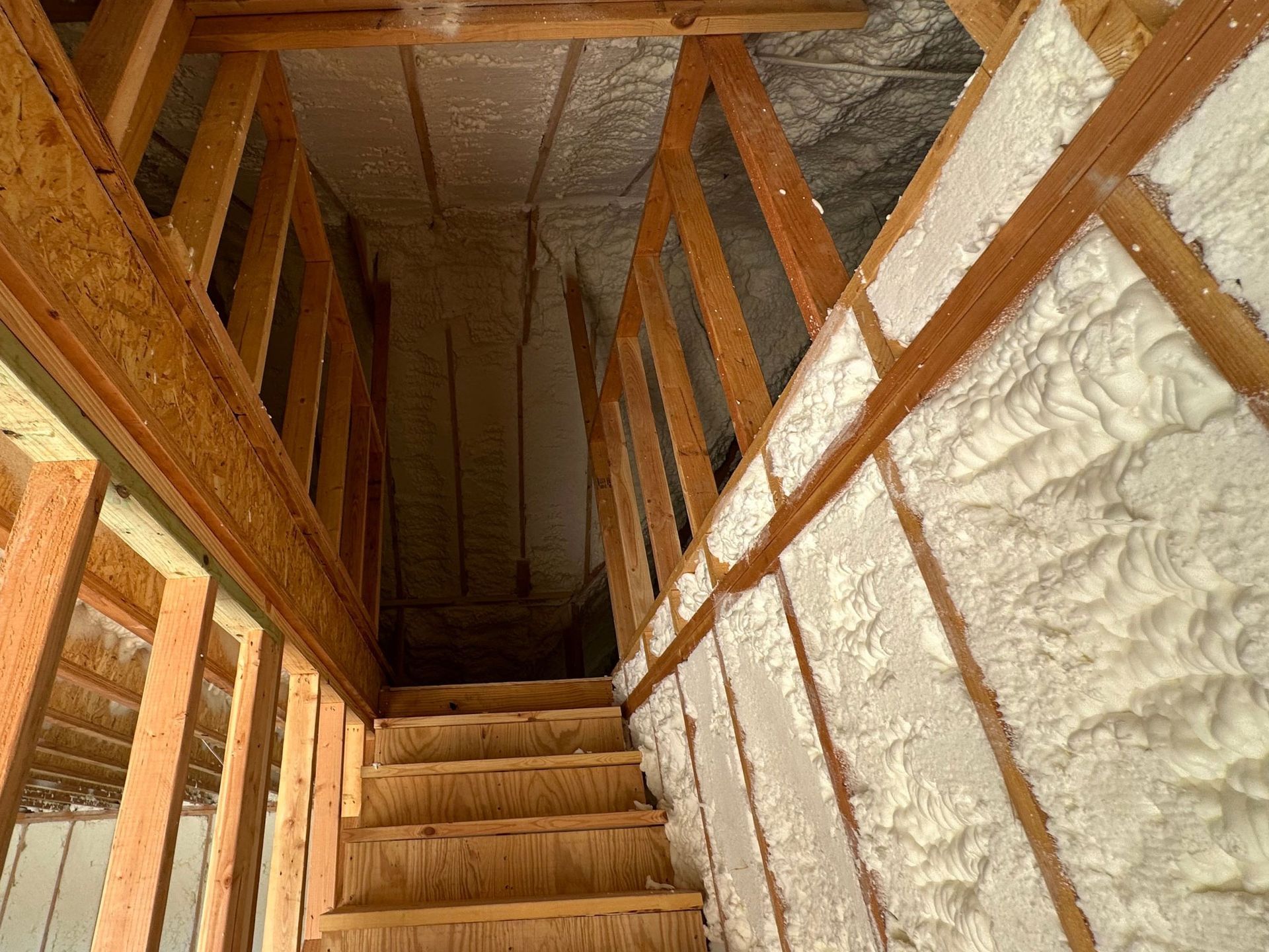 Wooden staircase in an attic, with spray foam insulation on the walls.