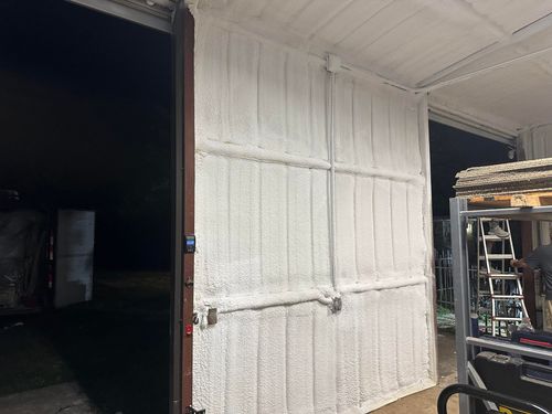 White insulation sprayed on the interior walls and ceiling of a building. A door is open to the left, and a ladder is to the right.