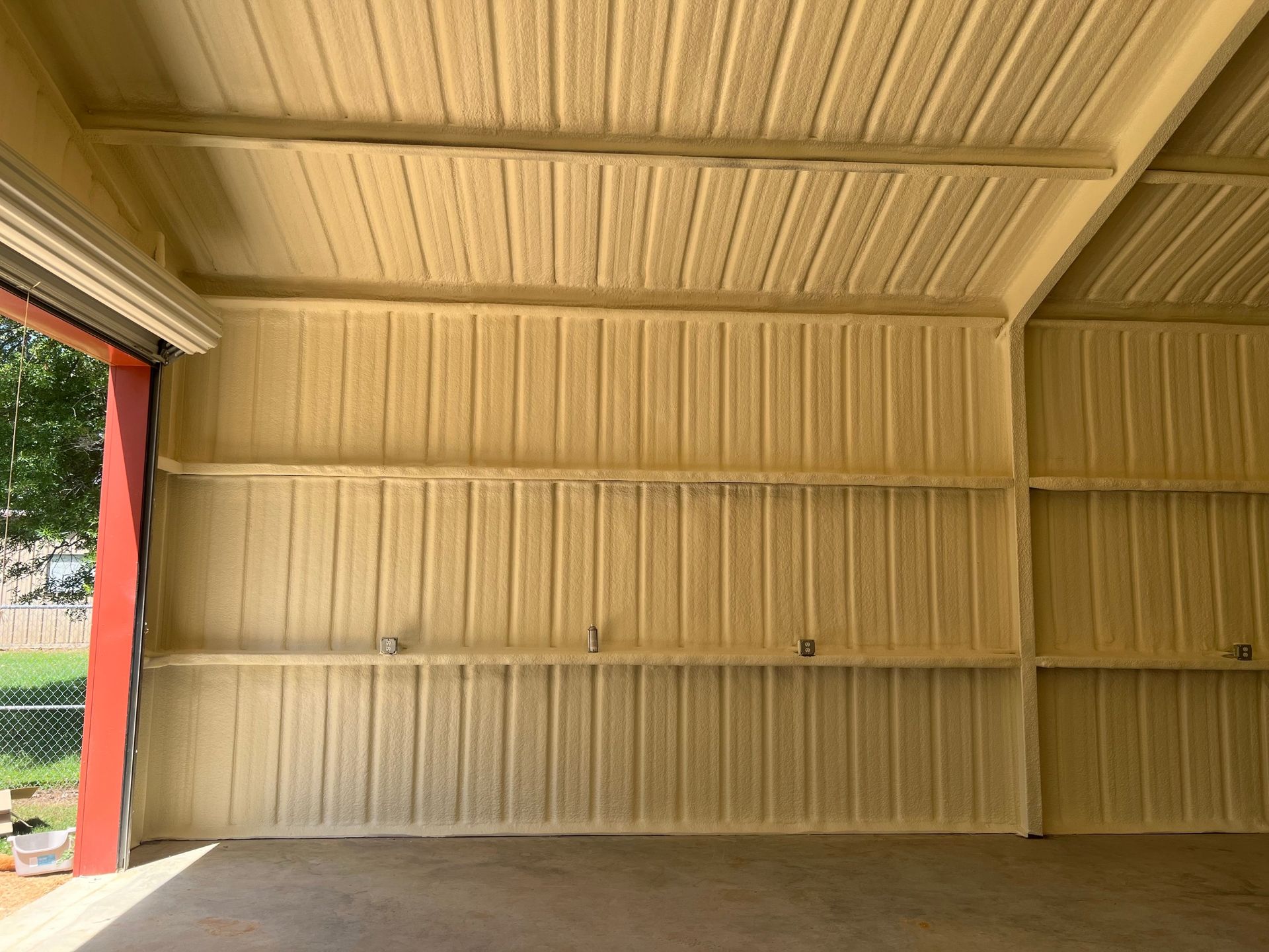 Interior view of a garage with spray foam insulation on the walls and ceiling; tan colored.