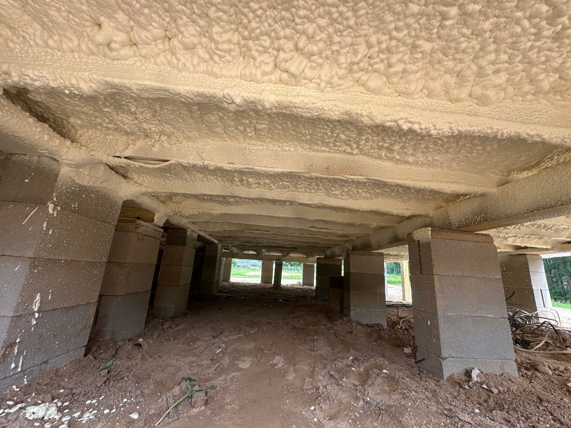Underside of a raised concrete structure on cinder block supports, with foam insulation visible on the ceiling.