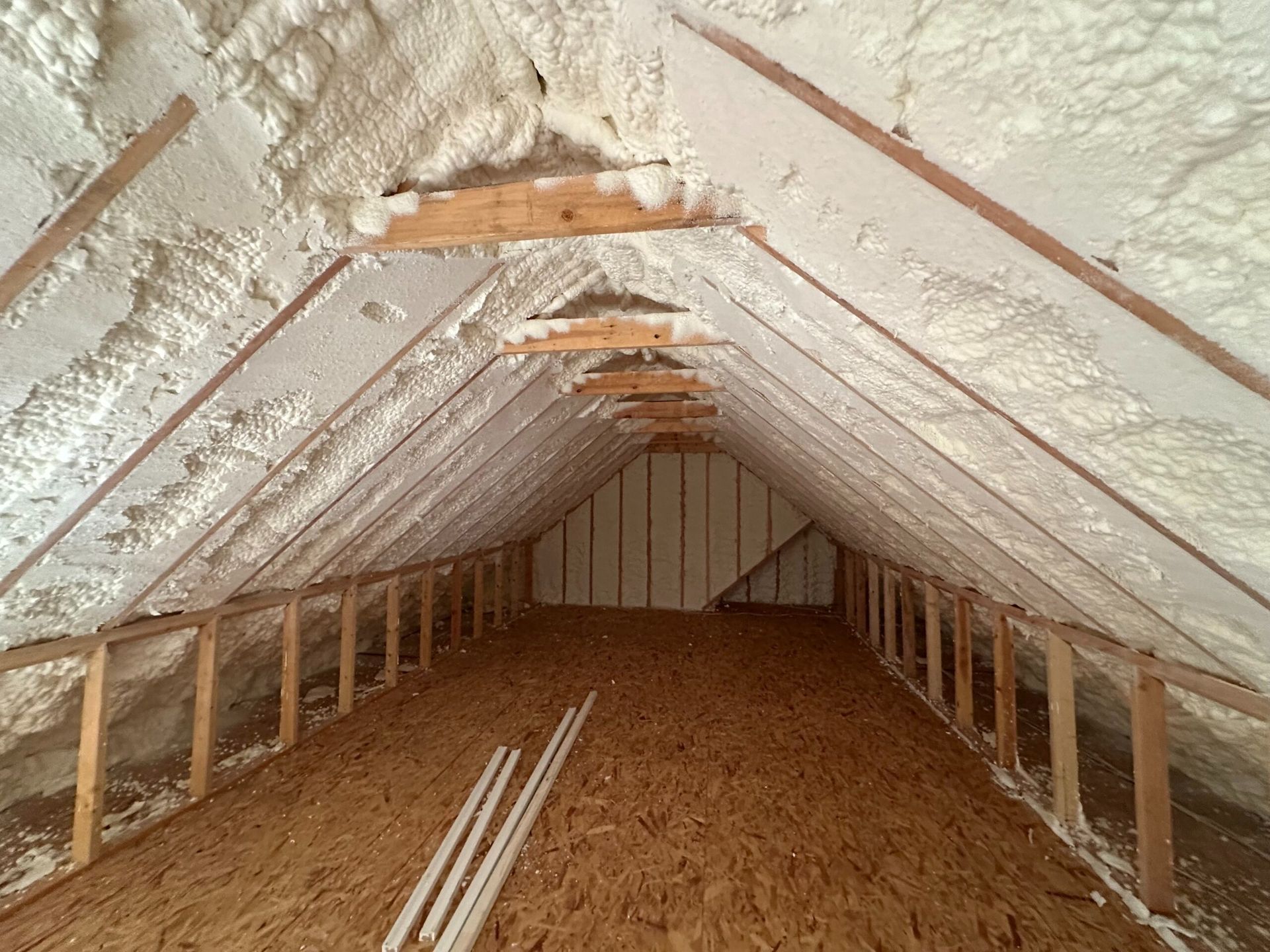 Attic interior with spray foam insulation on the roof and a wooden floor.