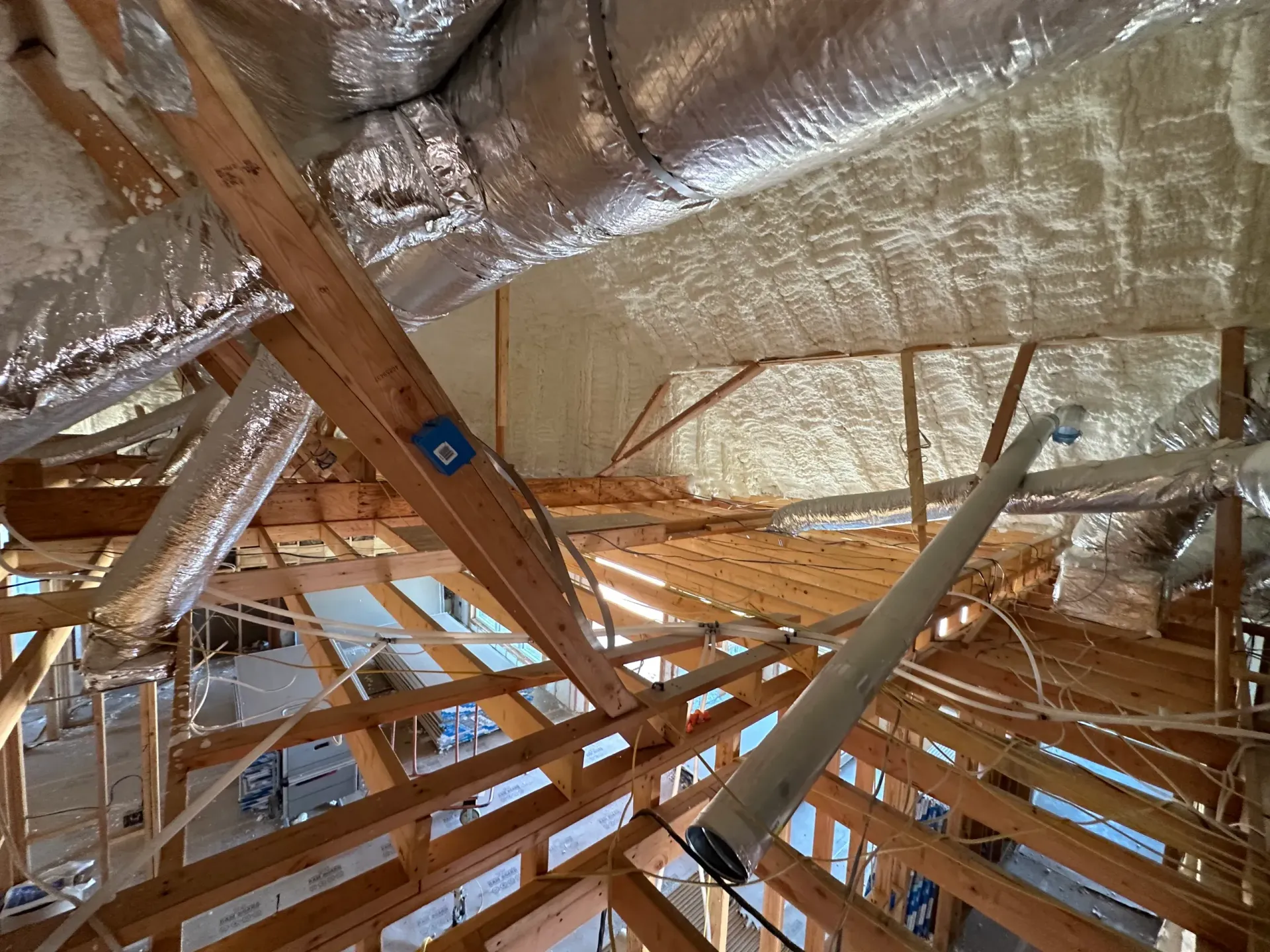 Attic with exposed wooden beams, ductwork wrapped in foil, and spray foam insulation.