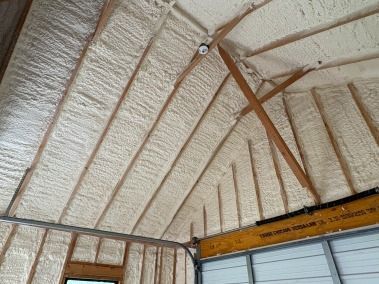 Attic rafters covered in light tan spray foam insulation, with exposed wood beams.