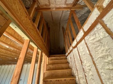Wooden staircase leading up into a dark attic, framed by insulated walls and ceiling.