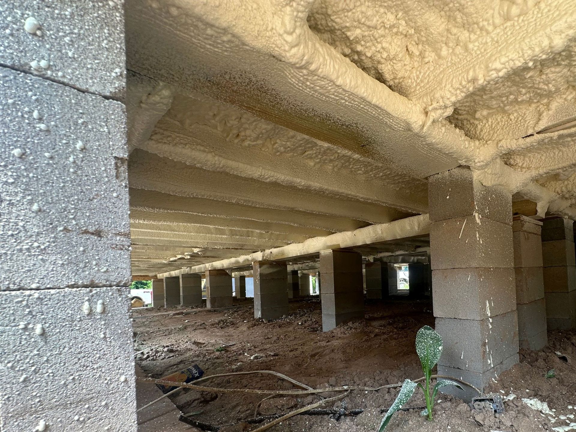 Underside of a house foundation; concrete blocks and wood beams are insulated with spray foam.