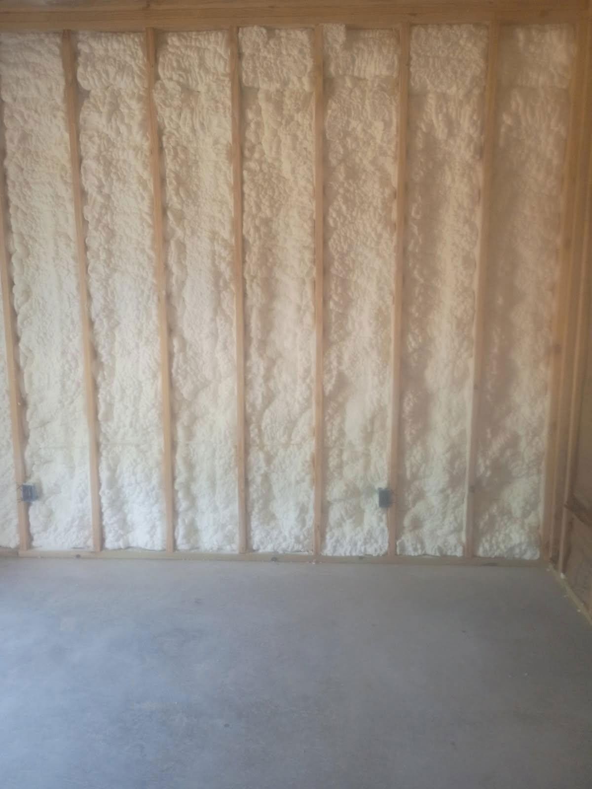 Wall of wooden studs filled with foamy insulation, against a concrete floor.