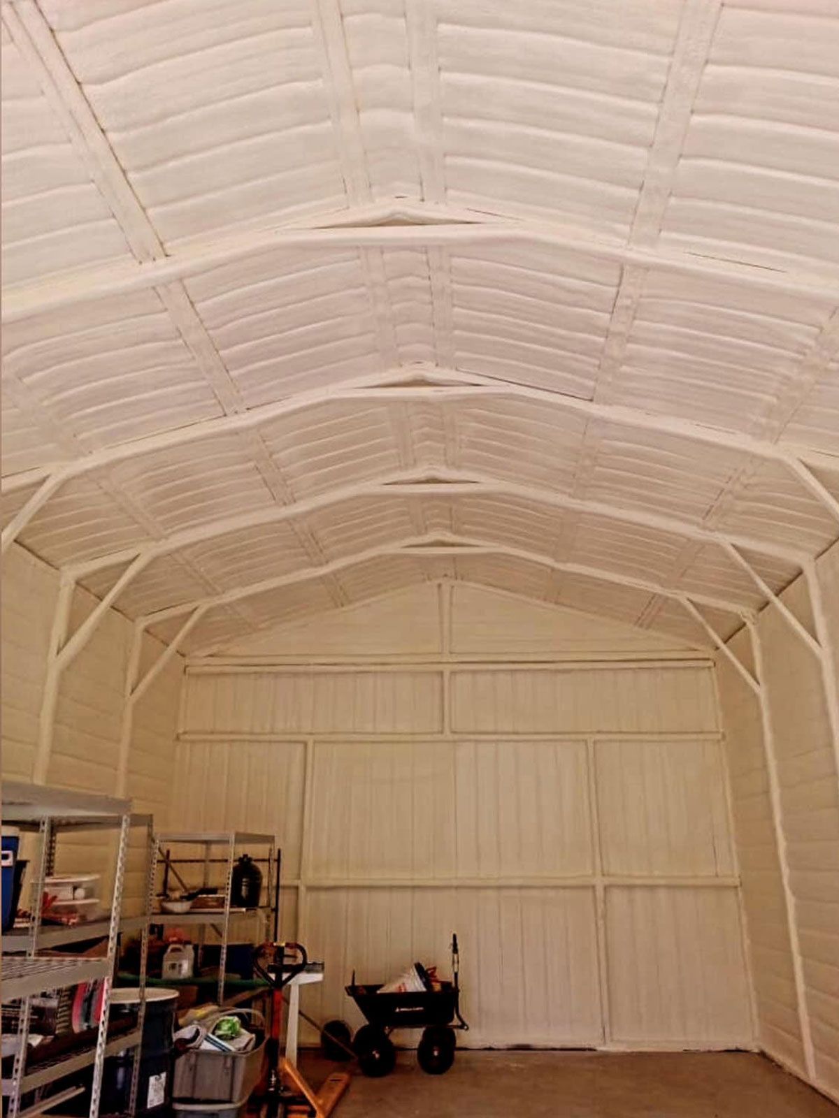 Interior of a white shed with metal framing and a concrete floor. Shelves and tools are visible.