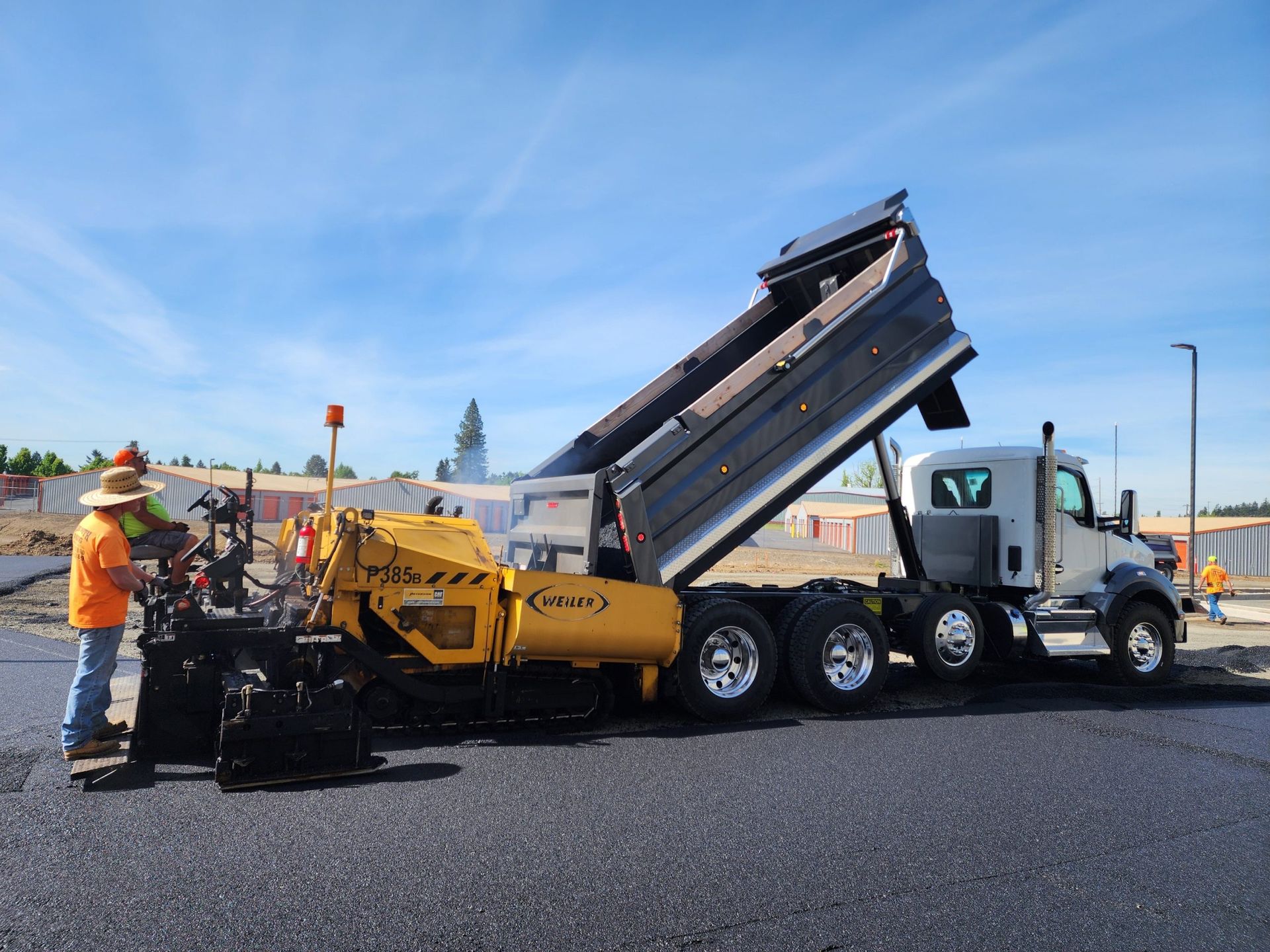 A dump truck is being loaded with asphalt at a construction site.