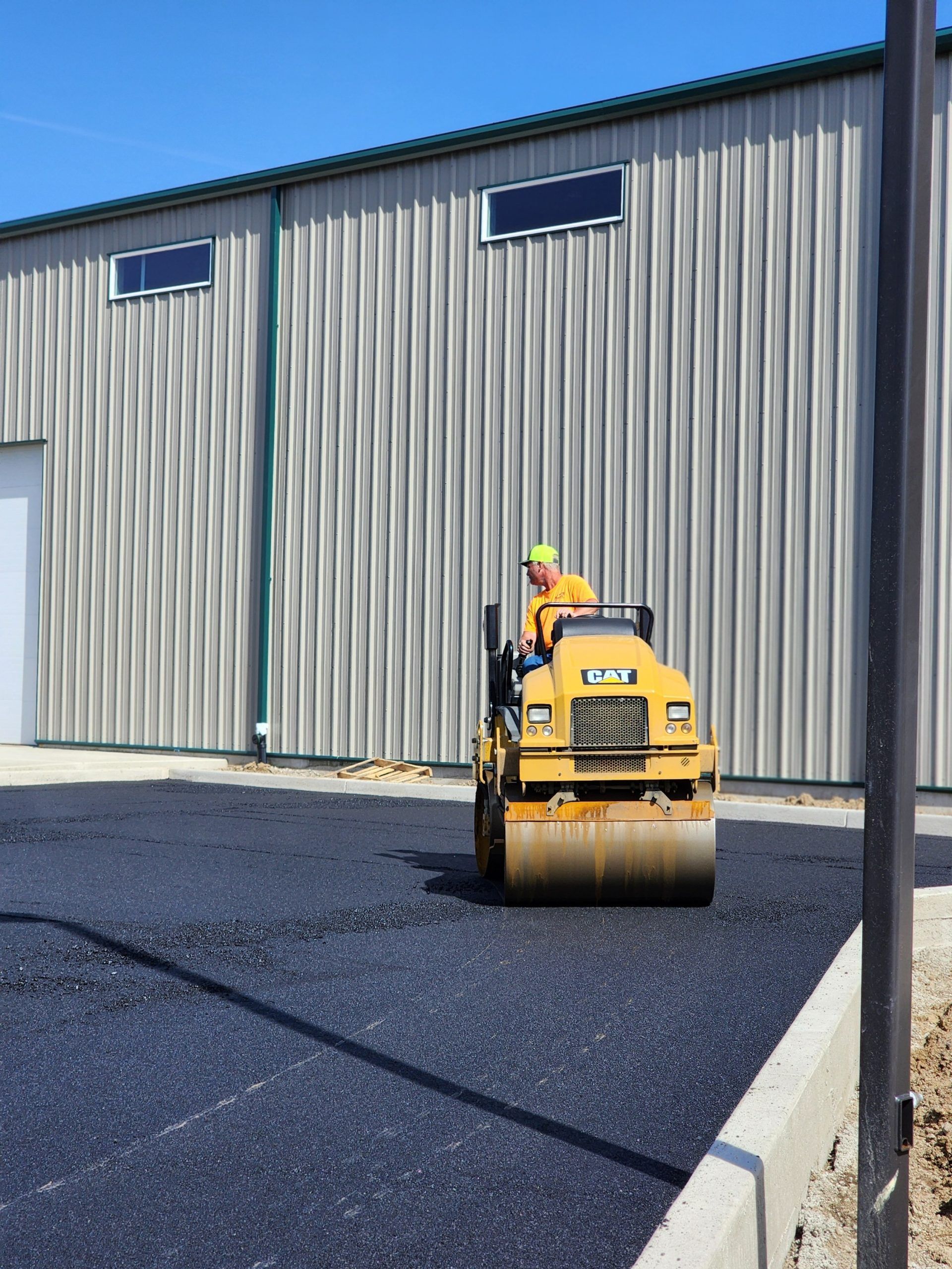 A man is driving a yellow roller in front of a building