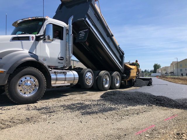 A dump truck is being loaded with asphalt on a construction site