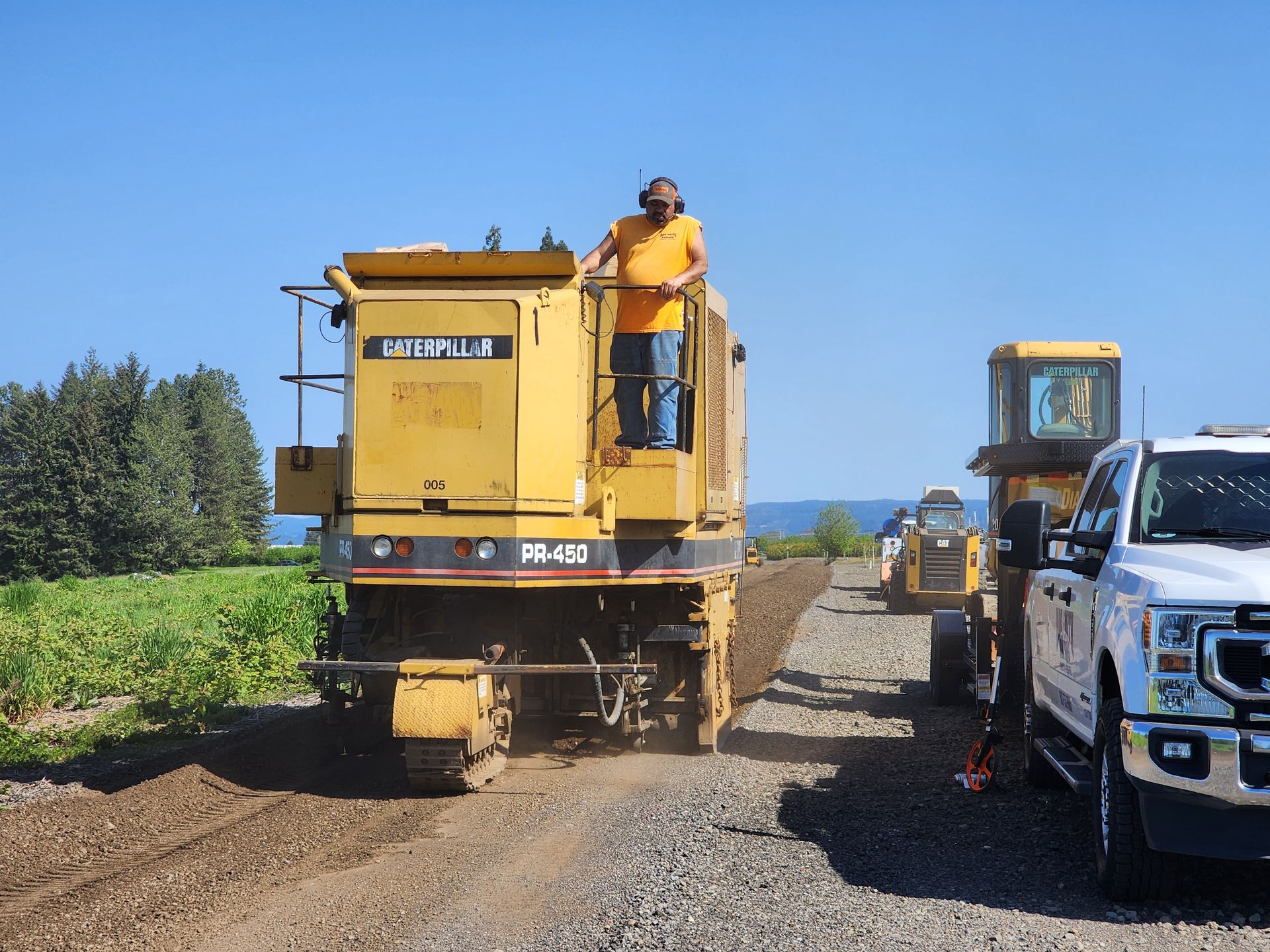 A man in an orange shirt is standing on top of a yellow machine.
