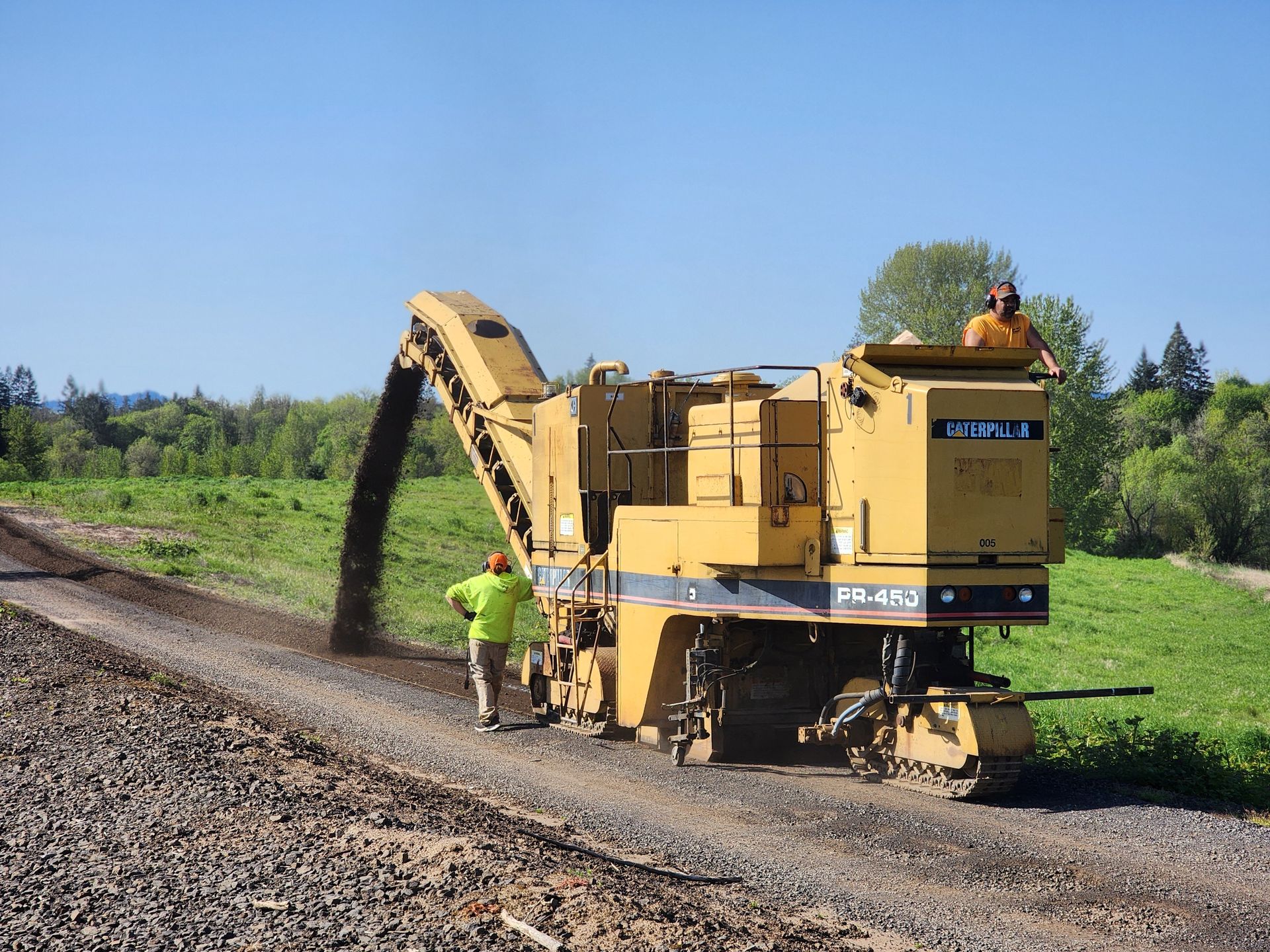 A man is standing next to a machine that is laying gravel on a road.