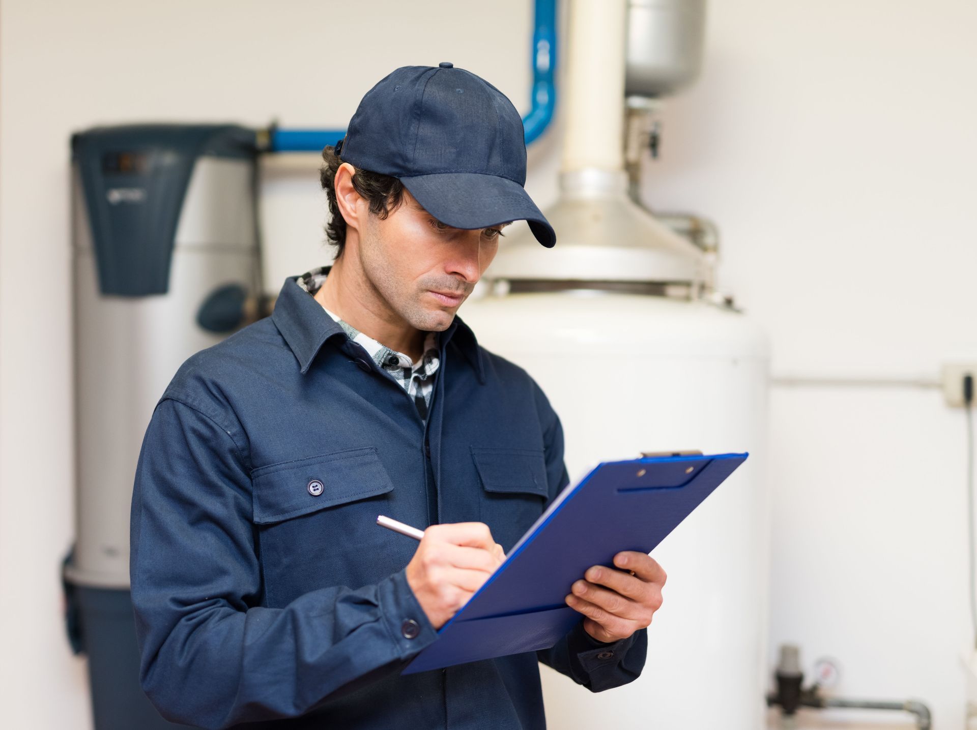 Technician in blue uniform and cap writing on a clipboard in an industrial room