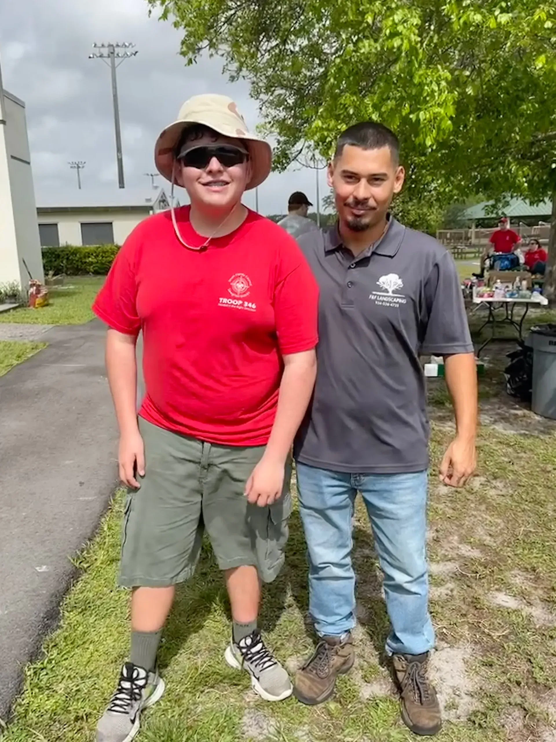 A boy in a red shirt is standing next to a man in a gray shirt.