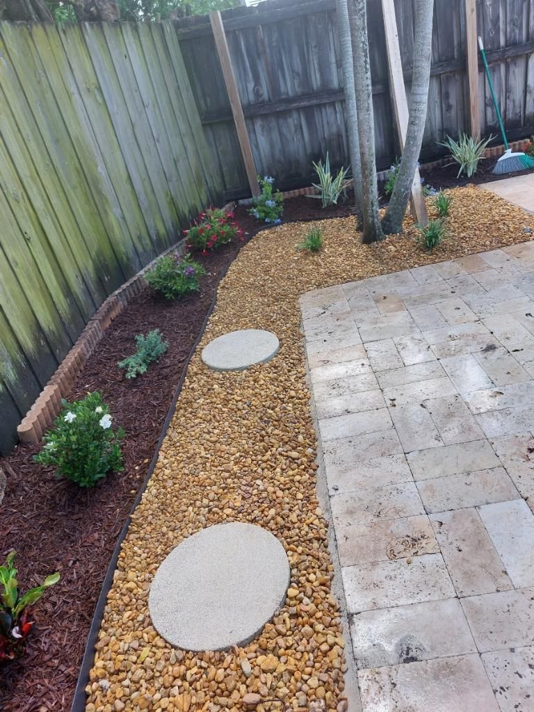 A garden with a fence and a walkway filled with rocks and plants.