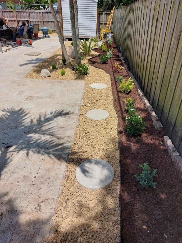 A backyard with a fence and a lot of plants and rocks.