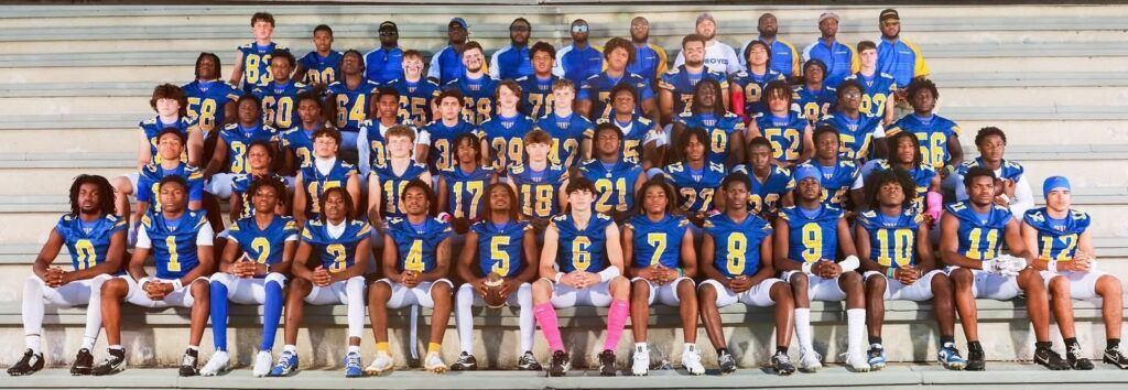 A large group of people, football team, seated on bleachers. Blue and gold uniforms.