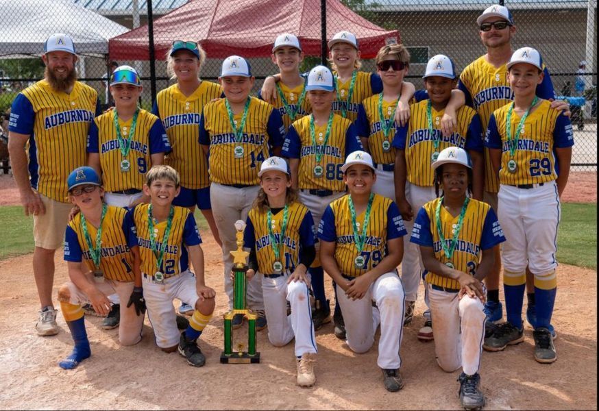 Baseball team posing with trophy; blue and yellow uniforms, outdoors.