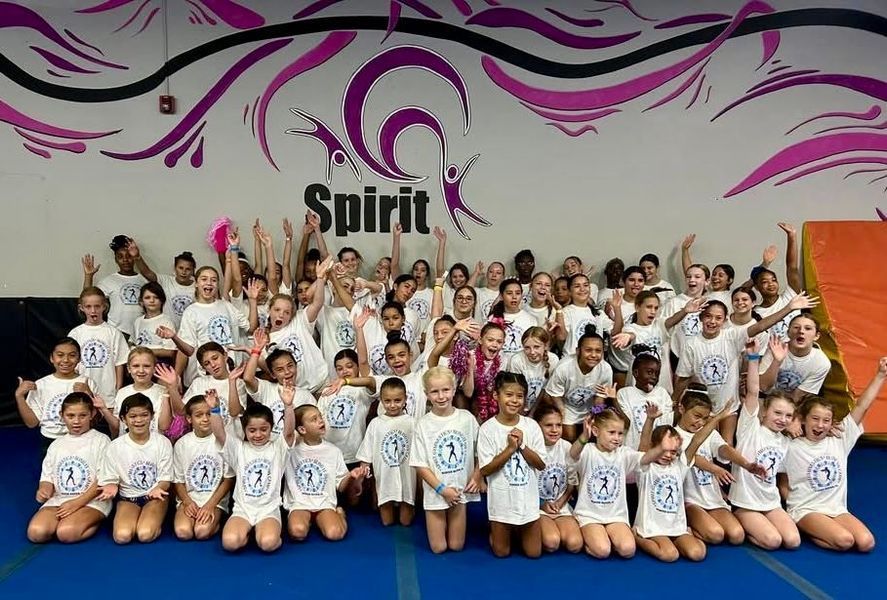 Group of kids in white shirts with arms raised in a gym with