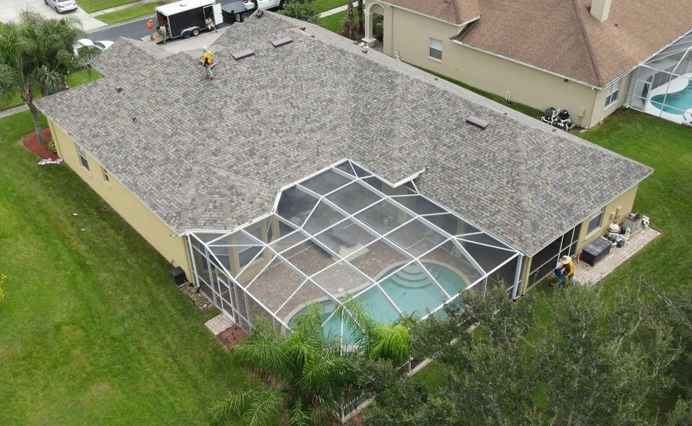 Aerial view of a house with a gray shingled roof, pool with screen enclosure, and green lawn.