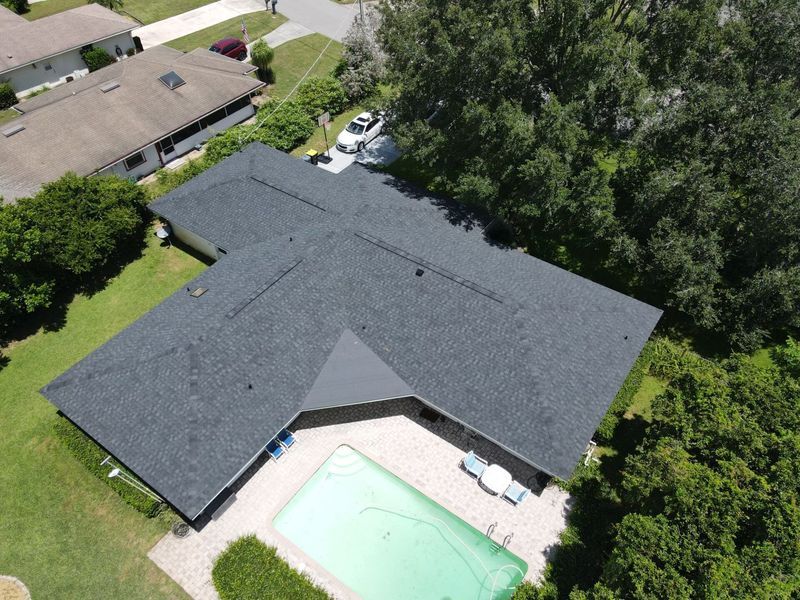Overhead view of house with dark gray roof, pool, and surrounding greenery.