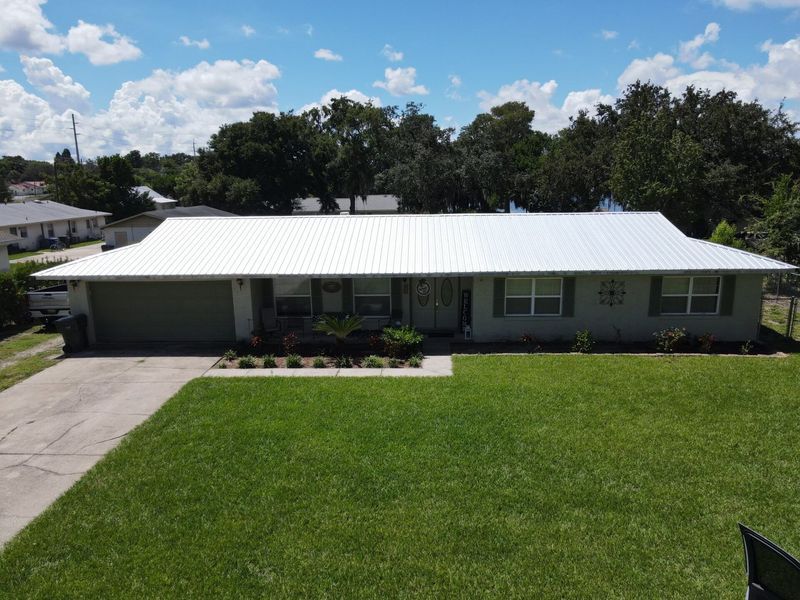 Gray house with a white metal roof, green grass, and a clear sky.