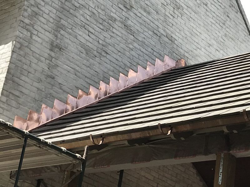 Copper flashing on a tiled roof, brick wall background. Scaffolding below.
