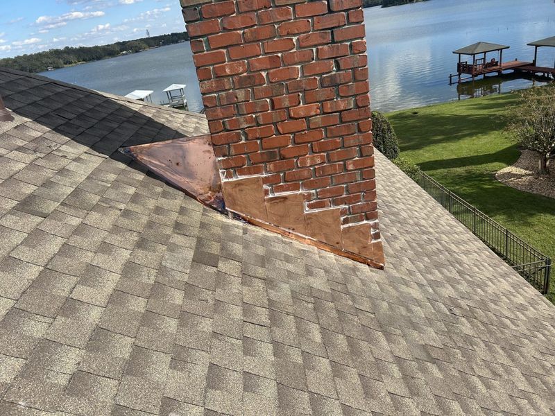 Brick chimney on a shingle roof with copper flashing, lake in the background.